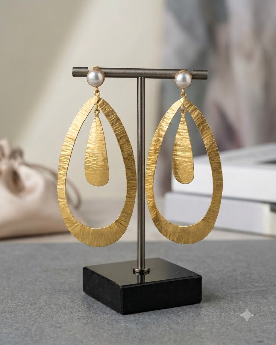 Pair of hammered matte gold teardrop earrings with freshwater pearls hanging on a stand